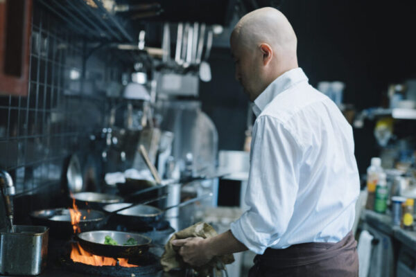 厨房でフライパンを使って料理をする料理人を写した写真
